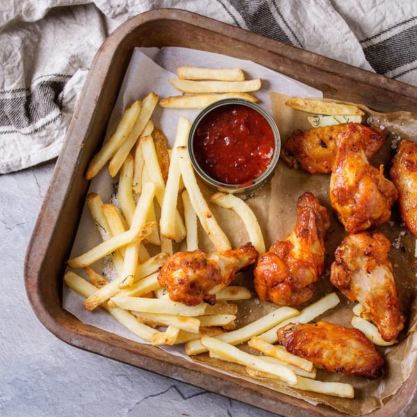 Crispy chicken wings with french fries and a side of ketchup in a rustic metal tray.