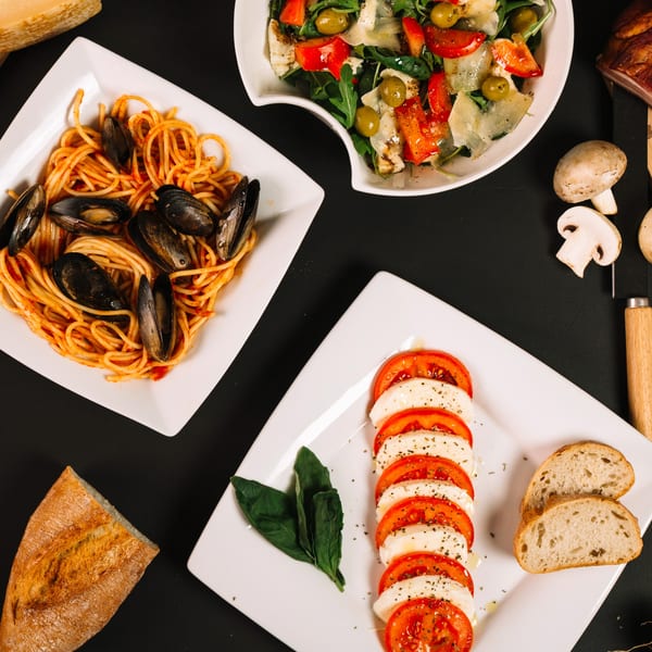 Overhead view of Italian dishes: mussels spaghetti, Caprese salad, and a green salad with bread.